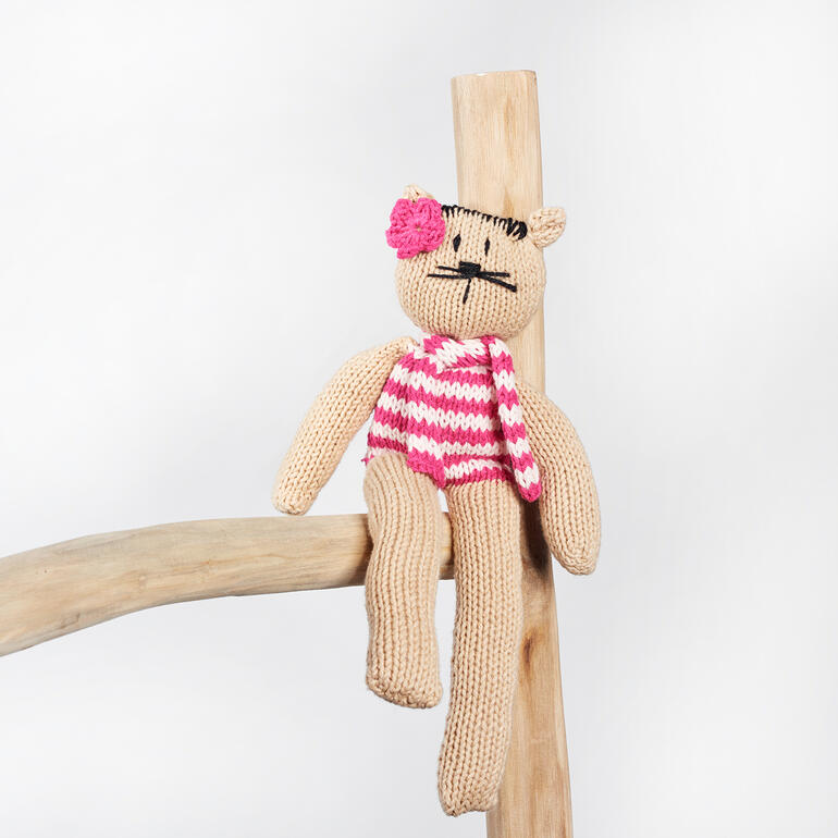 Schlenkerkatze mit buntem Schal, auf einem Holzstamm sitzend.