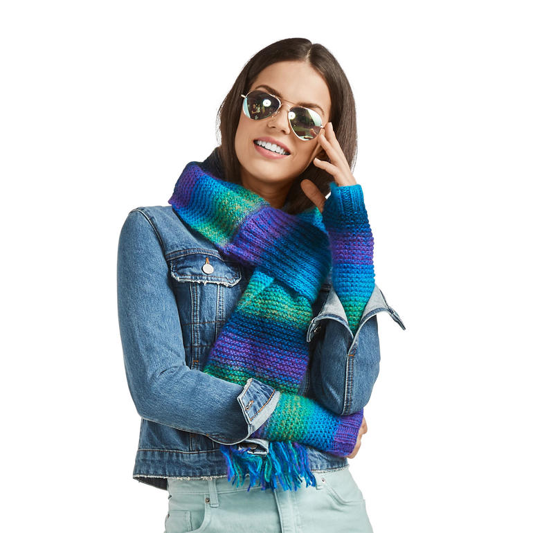 Dame mit buntem Schal und Pulswärmern aus Scala, trägt Sonnenbrille und lächelt.