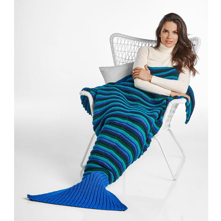 Frau in mehrfarbigem Schlafsack Meerjungfrau sitzt auf einem Korbstuhl, entspannt.