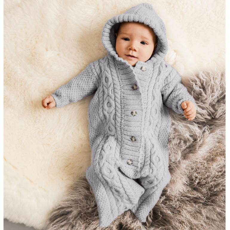 Baby im grauen Schlafsack mit Kapuze und Knöpfen auf einem flauschigen Untergrund.