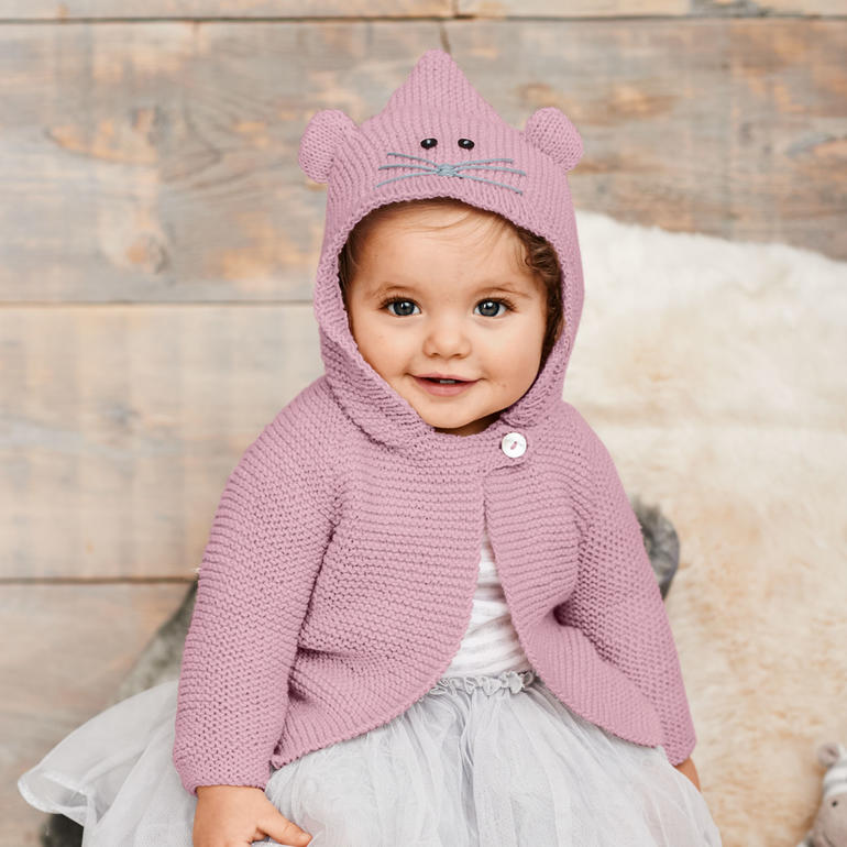 Baby in rosa Jacke mit Ohren, sitzt und lächelt auf Holzgrund.
