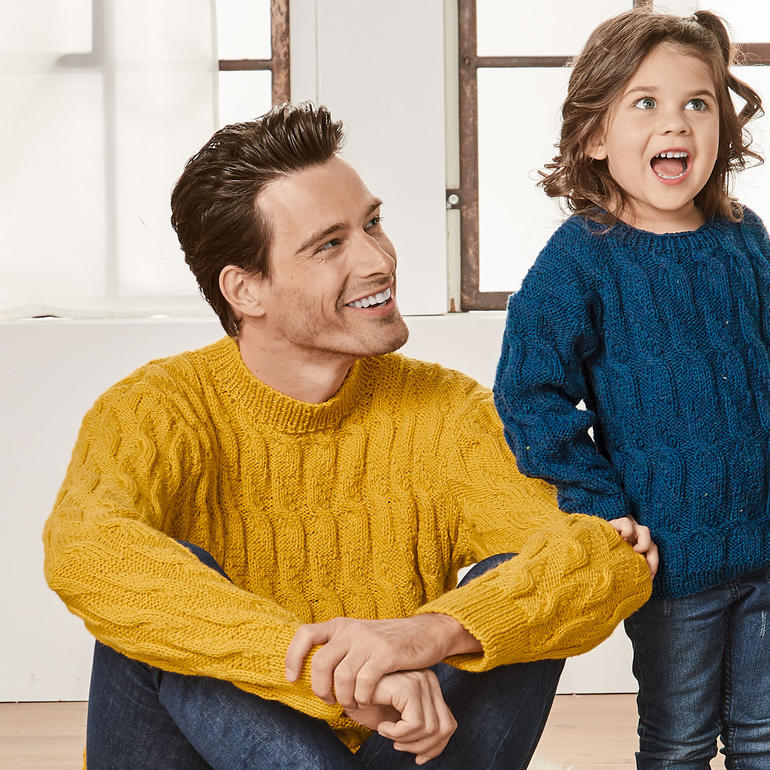 Vater und Kind in gemusterten Pullovern, fröhlich lächelnd in einem Innenraum.