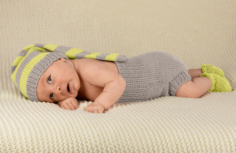 Baby-Set mit geringeltem Outfit und Mütze, liegend auf einer weißen Decke.