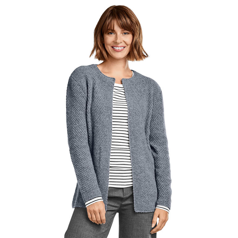 Dame in grauer Kaschmirjacke, freundlich lächelnd vor neutralem Hintergrund.