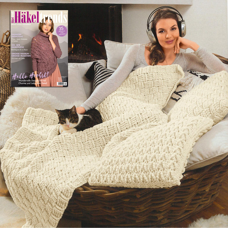 Häkeldecke und -kissen aus Merino Dick, Frau sitzt auf Sofa mit Katze.