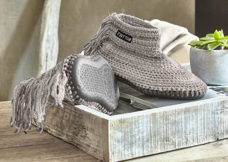 Botties aus grauer Landwolle auf einem Tisch mit Pflanzen