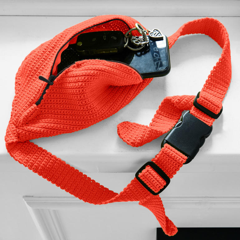 Gehäkelte Gürteltasche in leuchtendem Orange mit Schlüssel und schwarzem Handy.