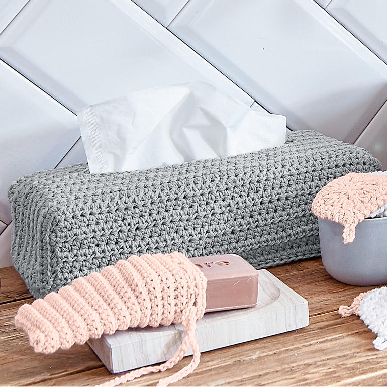 Grau gehäkelte Zupftuchboxhülle mit Taschentuch auf einem Holztisch.