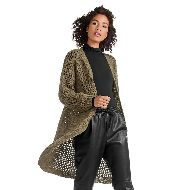 Damenmantel aus luftiger Spitze, lässige Pose vor einer weißen Wand.