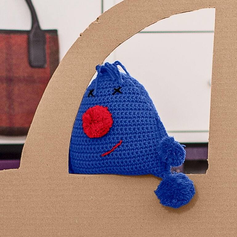 Blauer gehäkelter Kuschlkerl Kalle mit roter Nase im Auto.