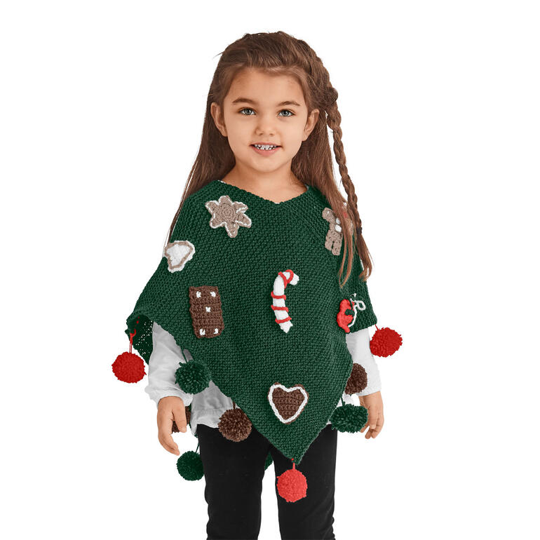 Mädchen trägt grünen Poncho mit weihnachtlichen Motiven und Pompons.