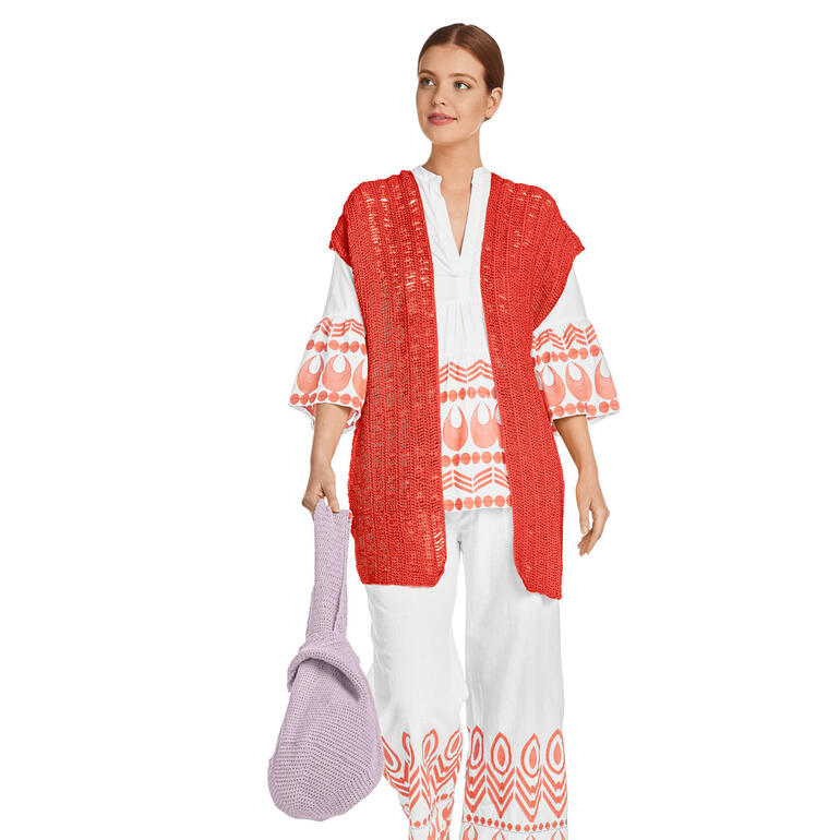 Frau mit rotem gehäkeltem Poncho und lila Beutel.