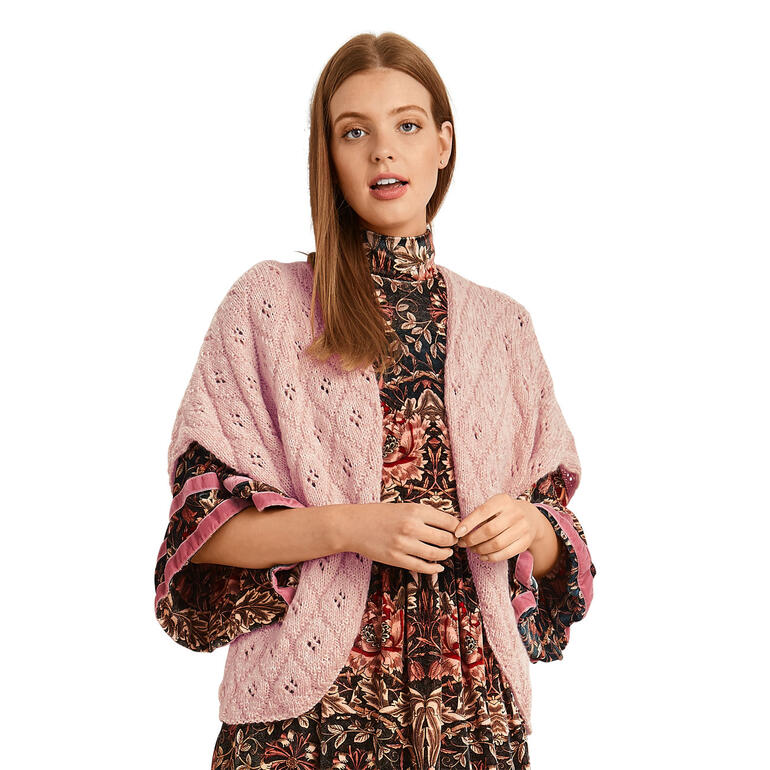 Frau mit rosafarbenem Bolero über einem gemusterten Kleid.