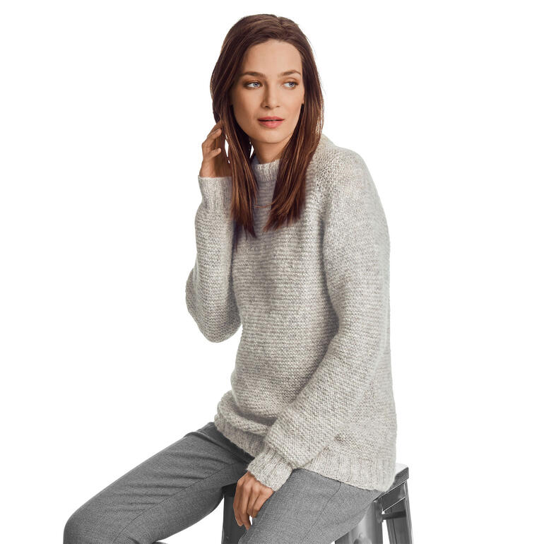 Frau sitzt in grauem Pullover aus Palazzo von Junghans-Wolle auf einem Hocker.