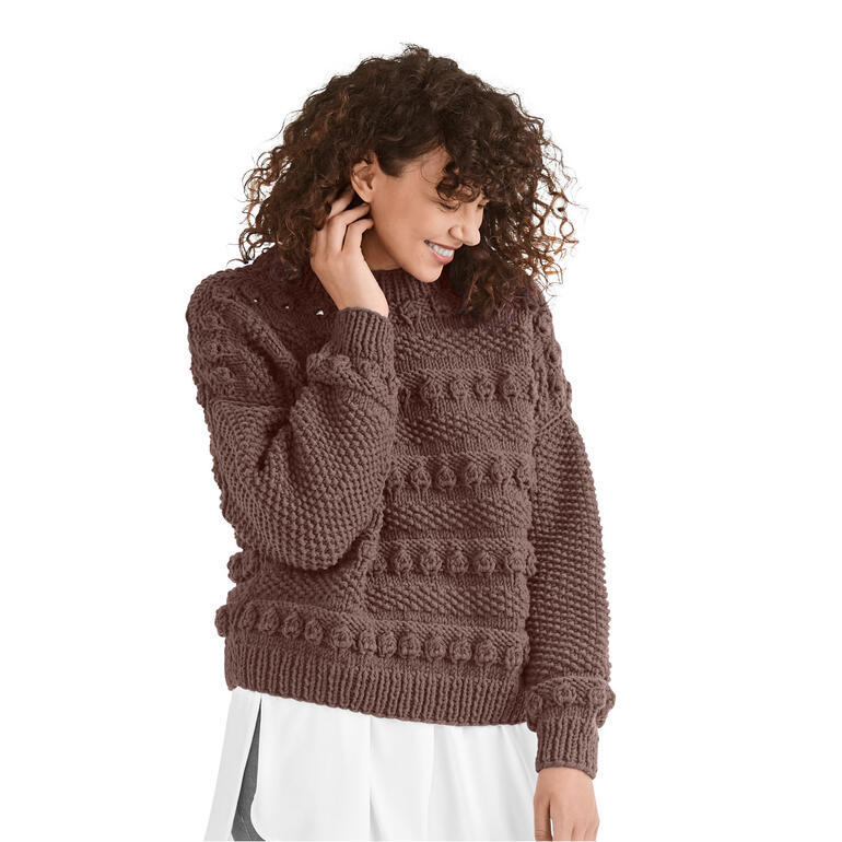 Frau mit lockigen Haaren trägt dunkle Pullover aus Merino Dick von Junghans-Wolle.