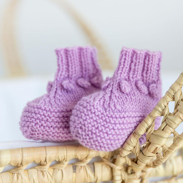 Lila Babyschühchen mit kleinen Bommeln auf einer Wickelunterlage.