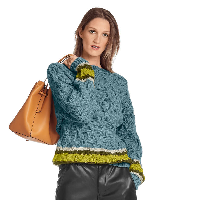 Frau trägt einen aquafarbenen Pullover mit strukturiertem Muster und gelben Streifen.