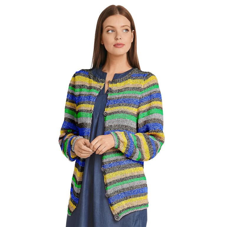 Frau in bunter Jacke aus Contrato sitzt in einem lässigen Outfit vor neutralem Hintergrund.