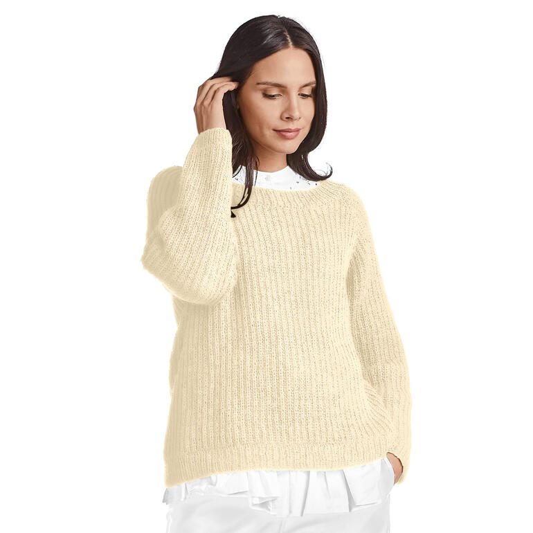 Frau in hellbeigem Pullover aus Onda posiert vor einem weißen Hintergrund.