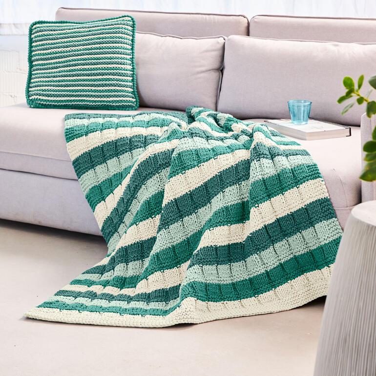 Gestreifte Decke und Kissen in Grüntönen auf einem Sofa.