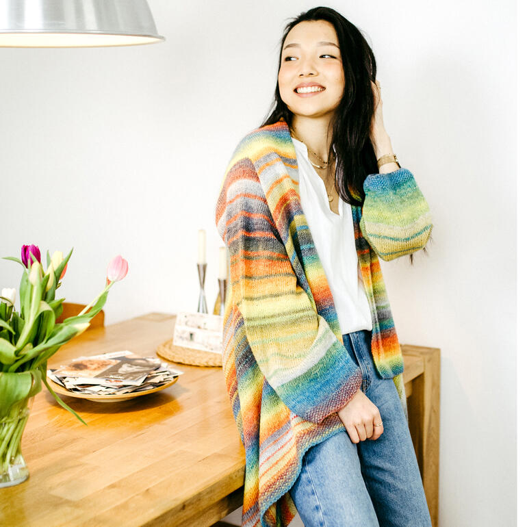 Frau in einem bunten Cardigan steht neben einem Tisch.