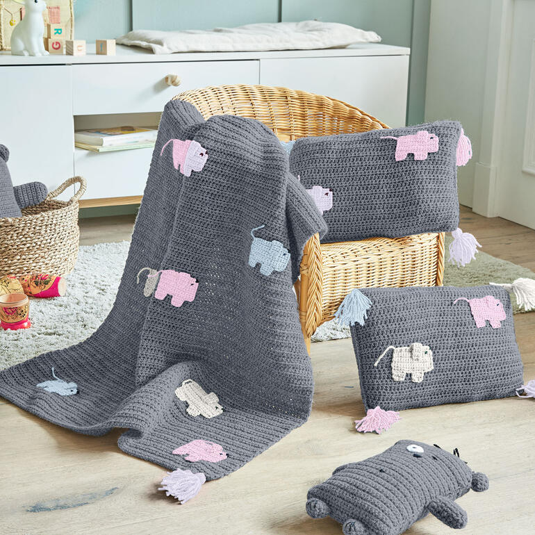 Grau gehäkelte Decke und zwei Kissen mit Tiermotiven.