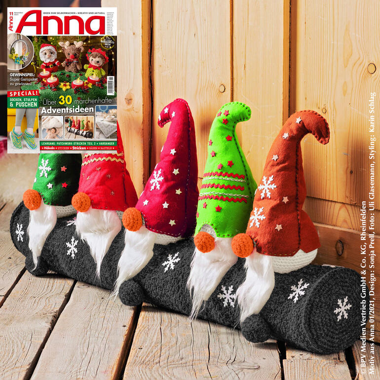 Bunte Zugluftstopper in Form von Weihnachtsmann-Figuren auf einer grauen Unterlage.