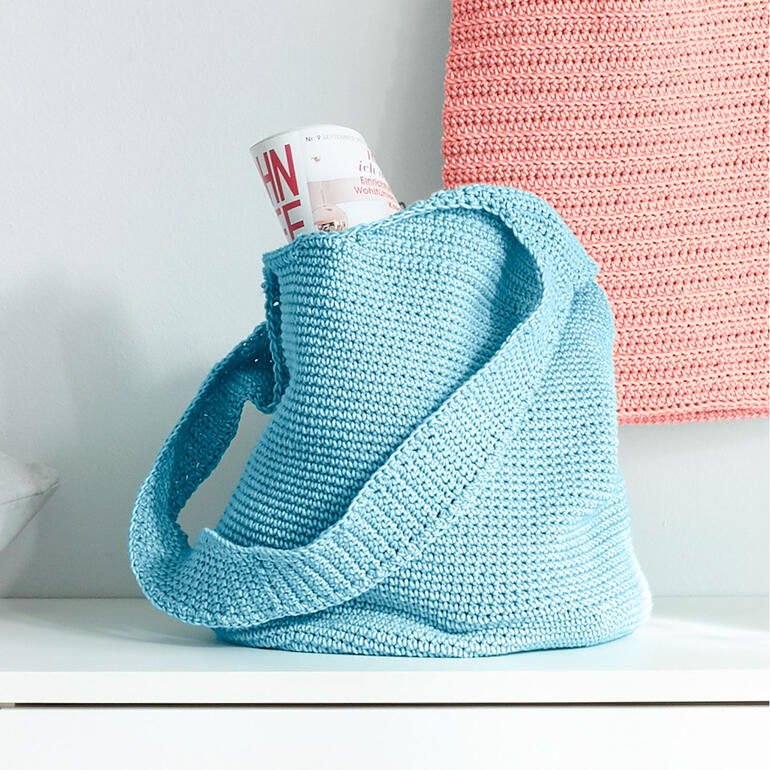 Häkeltasche in hellblau mit Inhalt auf einem Tisch.