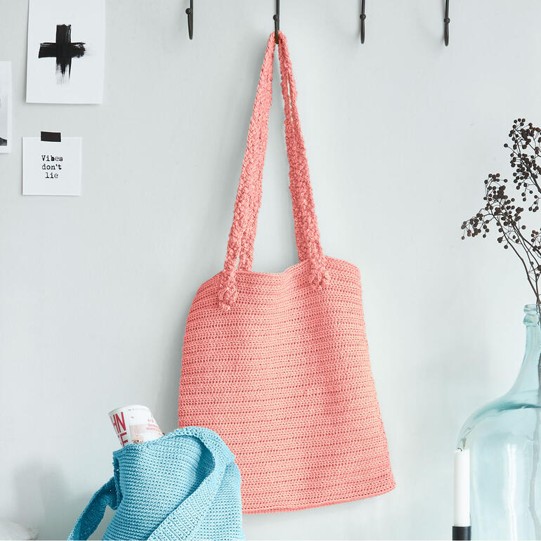 Rosa Häkeltasche hängt an einem Haken, dekorativ geflochten.