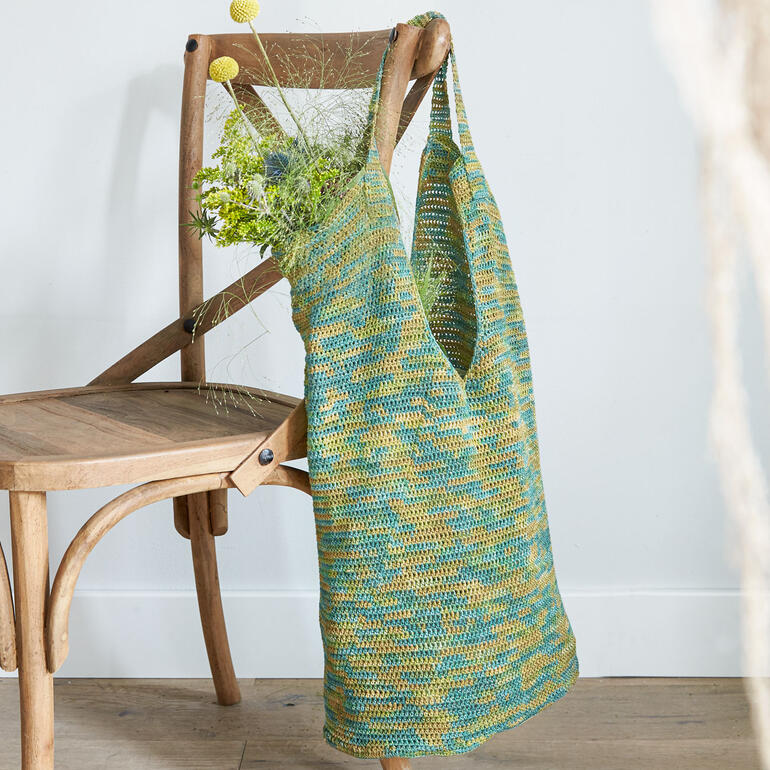 Häkeltasche aus Silka®, elegant drapiert über einen Holzstuhl.