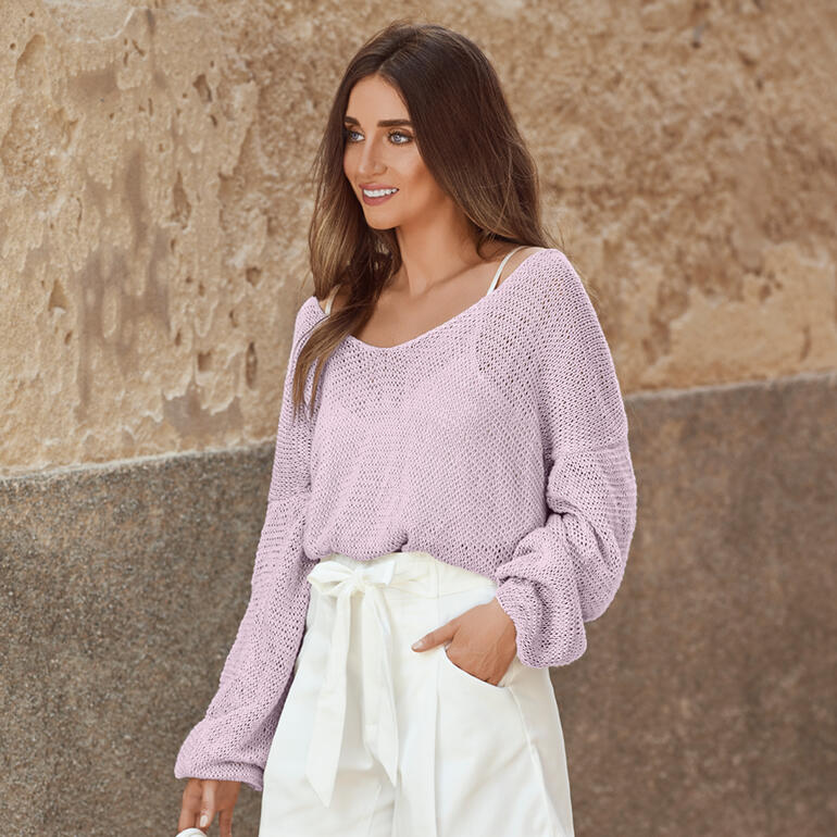 Frau trägt einen lila Pullover mit weitem Ausschnitt und lockeren Ärmeln in natürlicher Umgebung.
