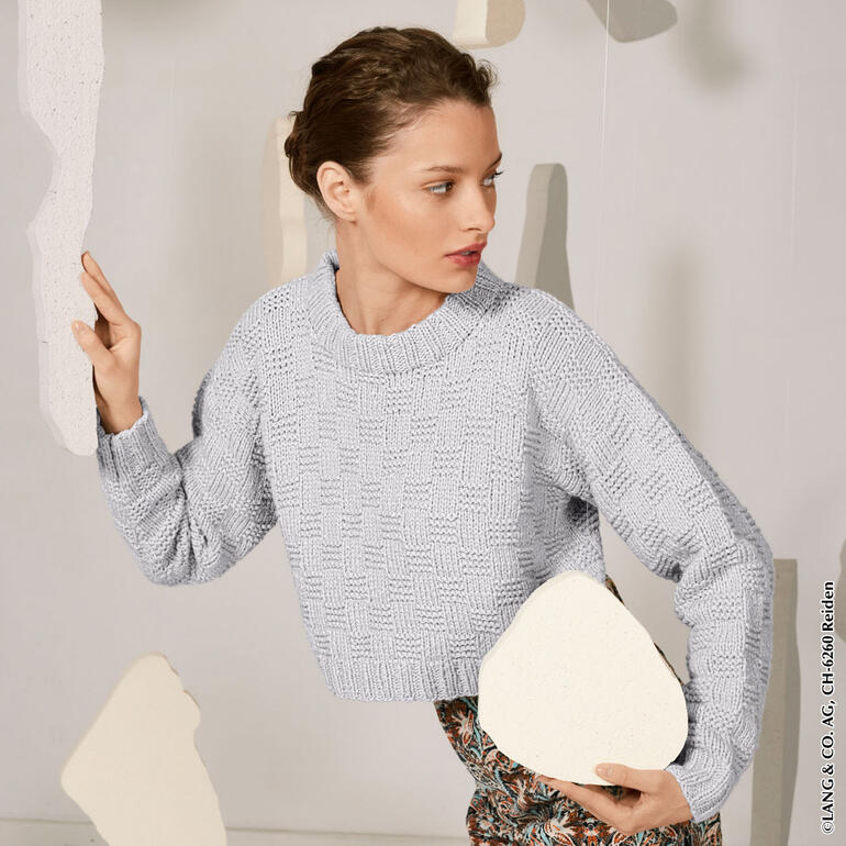 Frau in hellgrauem Pullover aus Honesty, posiert mit Felsen.