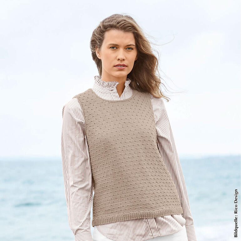 Frau in beigem Pullunder aus Essentials Organic Cotton am Strand.