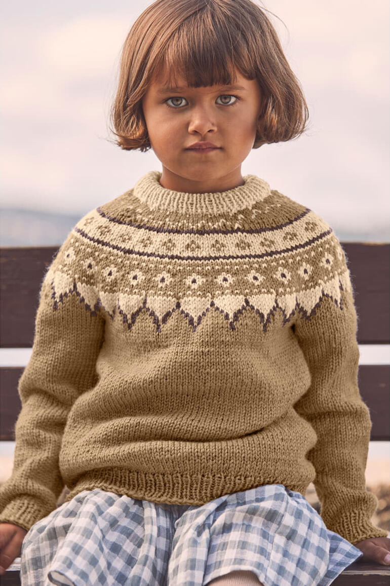 Kind in braunem Pullover mit rundem Kragen, schaut ernst zur Seite.