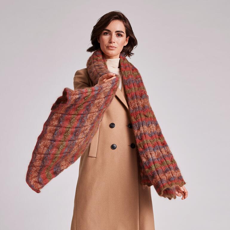 Frau mit Schultertuch aus meliertem Garn, Pose im Licht, lächelt.