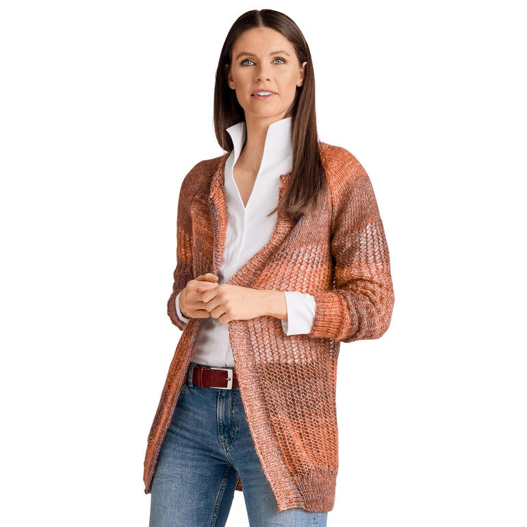 Frau in brauner Jacke aus grobem Garn steht lächelnd vor neutralem Hintergrund.