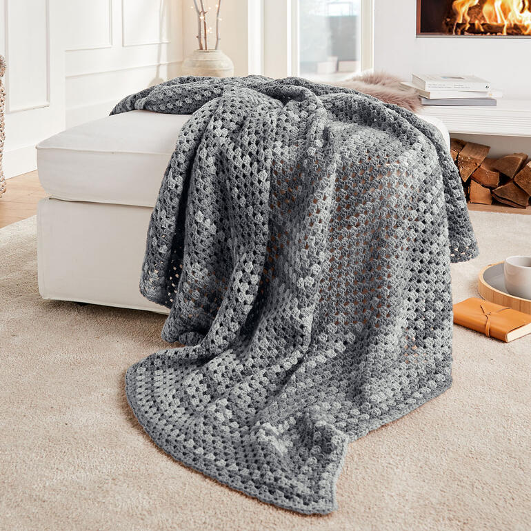 Gehäkelte Decke aus Cassandra Print in Grautönen auf einem Sessel.