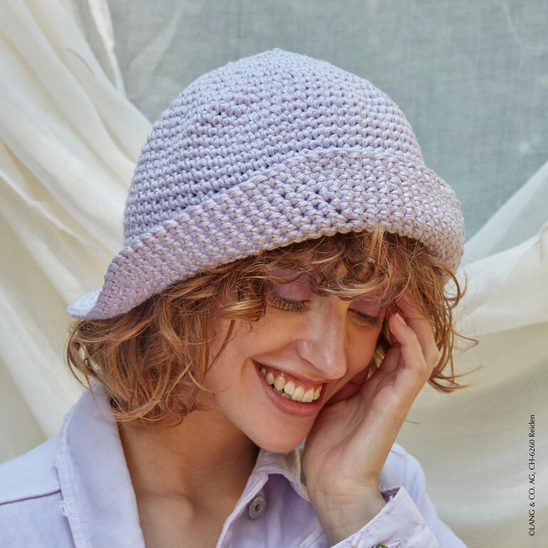 Lila gehäkelter Hut auf einer lächelnden Frau mit lockigem Haar.
