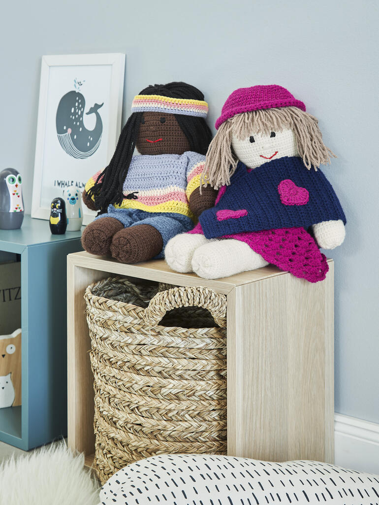 Gehäkelte Puppen Lilly und Polly aus Poco, sitzend mit unterschiedlichen Outfits.