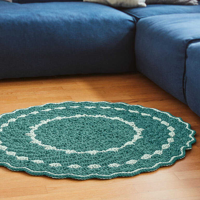 Runder gehäkelter Teppich in Grün und Beige auf Holzboden.