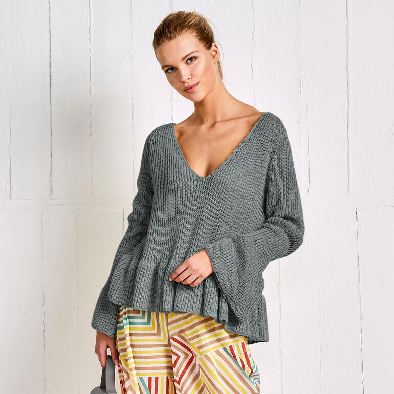 Frau in grauer Tunika mit vollem Saum und weitem V-Ausschnitt vor hellem Hintergrund