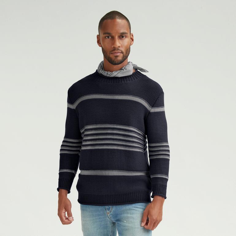 Mann in navy-blauem Pullover mit Streifenmuster vor hellgrauem Hintergrund