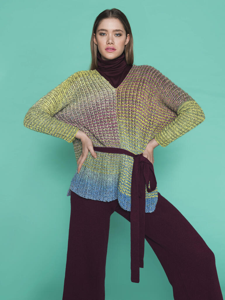 Frau in grünem Poncho mit Gürtel vor türkisfarbenem Hintergrund