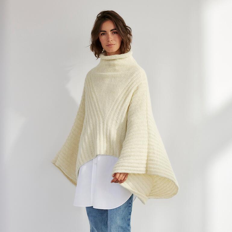 Poncho aus Palazzowolle in cremefarben, getragen von einer Frau im Stehen.