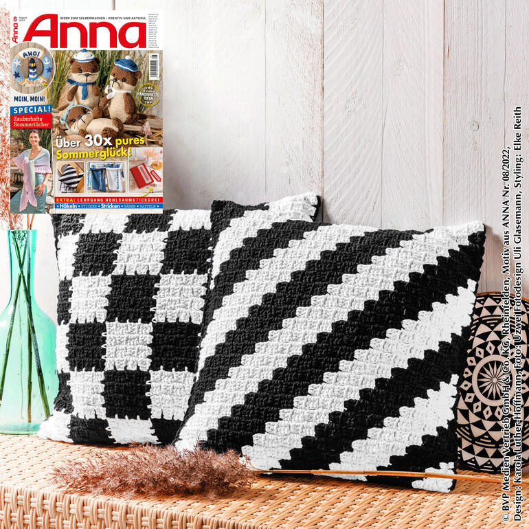 Häkelkissen in Schwarz und Weiß, geometrisches Design auf einem Holztisch.