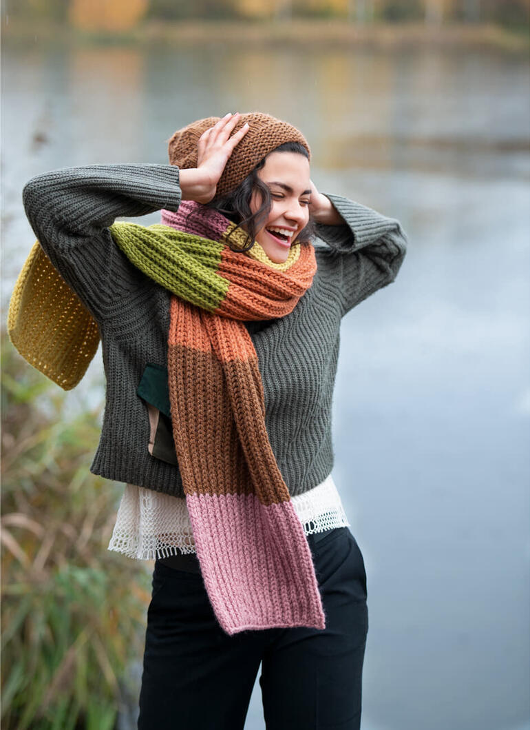 Frau mit buntem Schal und Mütze lacht glücklich im Freien.