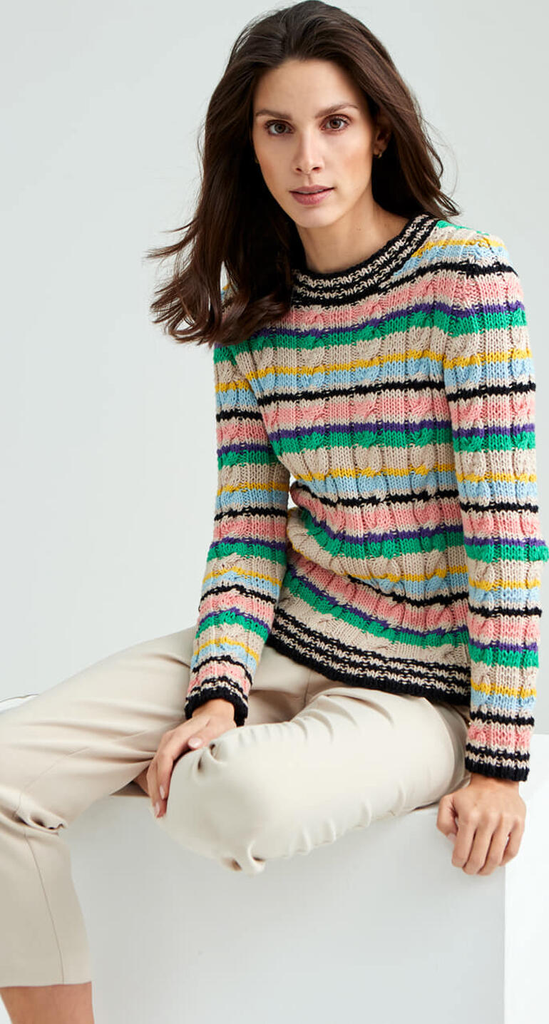 Bunter Pullover aus Cotonara mit Streifen, Frau sitzt auf einem weißen Block.