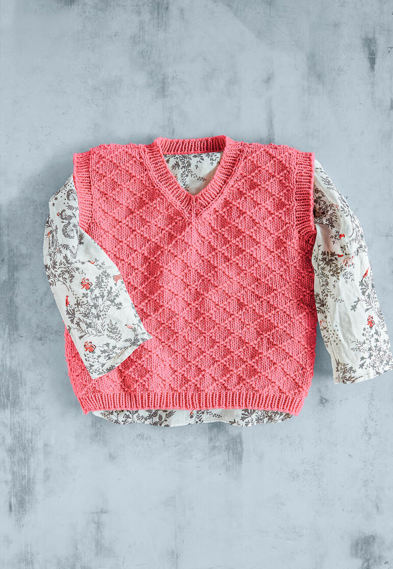 Rosa Kinderpullunder aus Recycle & Cotone, über einem blütenmuster Hemd drapiert.