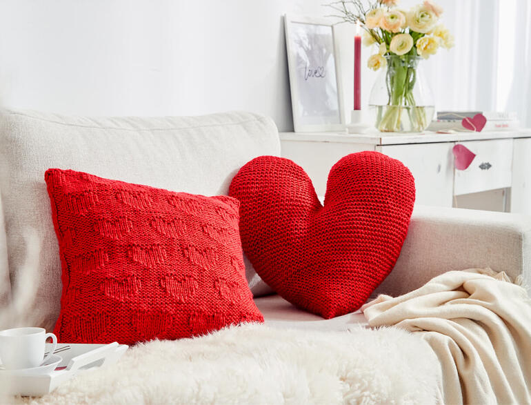 Herzkissen aus Enny, präsentiert auf einem Sofa mit einer dekorativen Kissen und Zugang zu einer Tasse.