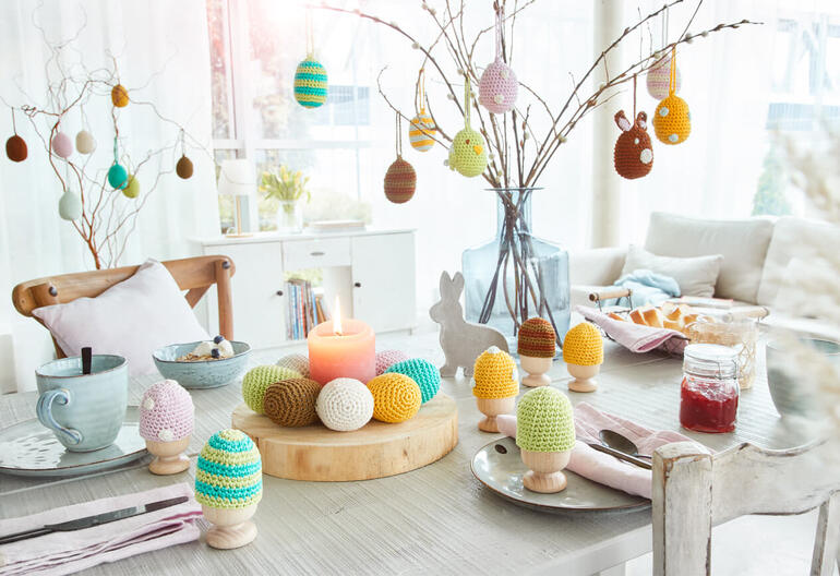 Eierwärmer-Kranz und dekorative Eier aus Cottonprima, auf einem festlich gedeckten Tisch.